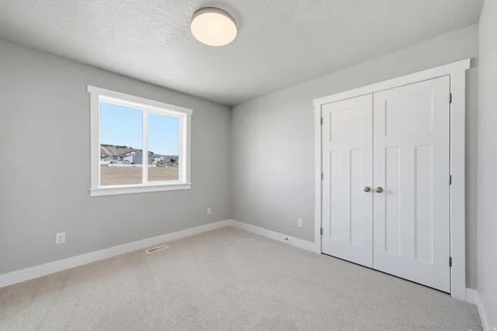 Neutral wall color, carpeted flooring, a window with white trim, and a double-door closet with paneling