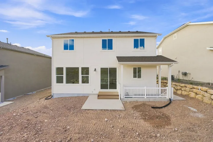 Two-story exterior with a covered patio, white railing, sliding glass door, and a retaining wall
