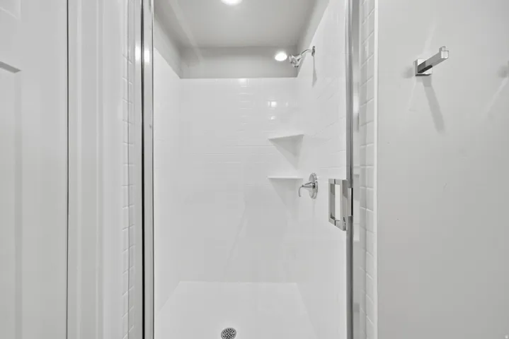 Modern shower enclosure featuring a frameless glass door, white subway tile surround with built-in shelving, chrome fixtures, and recessed ceiling lighting