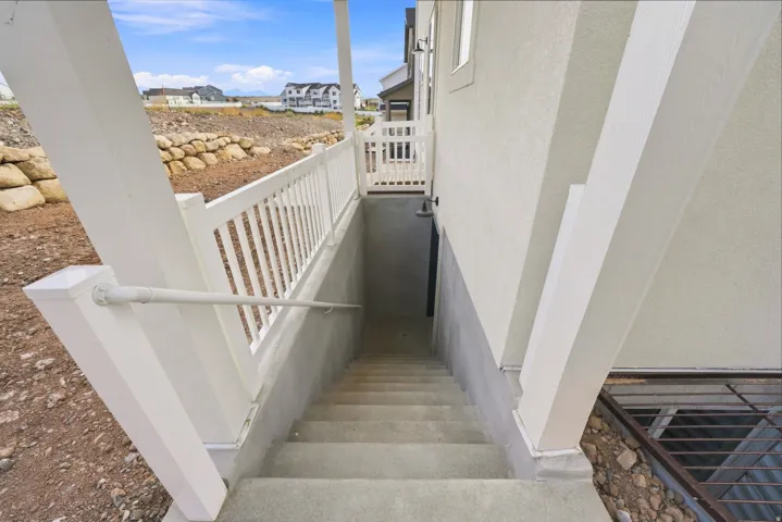 Exterior basement access with concrete stairs, white railing, and stucco siding
