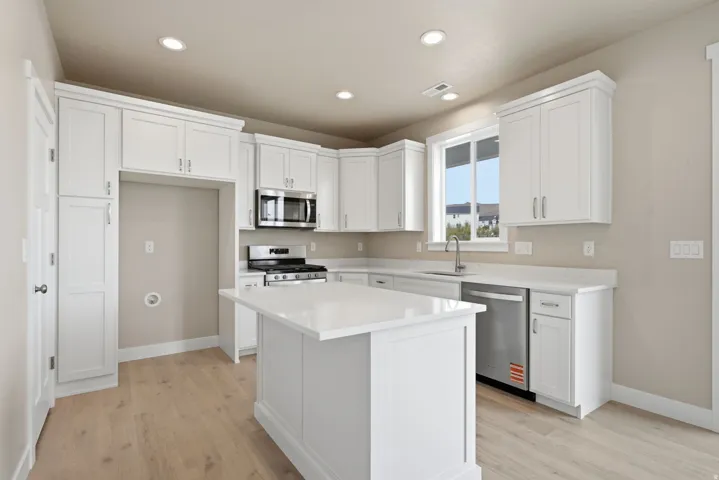 White cabinetry with crown molding, stainless steel appliances, light wood-finish flooring, recessed lighting, and a kitchen island with stone countertops