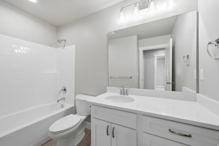 White subway tile shower surround with a built-in tub, single-sink vanity with white cabinetry, and a wide mirror with overhead lighting