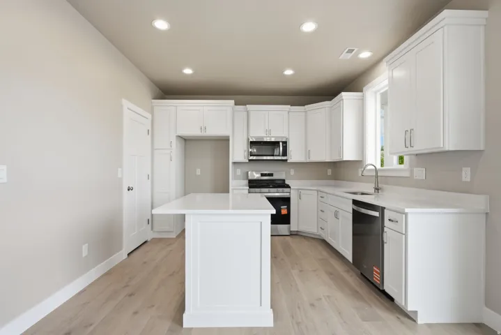 Kitchen featuring white cabinetry, a central island, stainless steel appliances, light-toned countertops, and wood-finish flooring