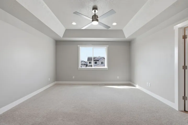 Tray ceiling with recessed lighting and a ceiling fan, neutral wall paint, window with white trim, and carpeted flooring
