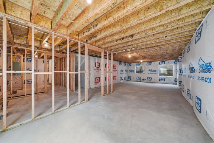 Unfinished basement with concrete flooring, framed interior walls, exposed ceiling joists, and multiple windows