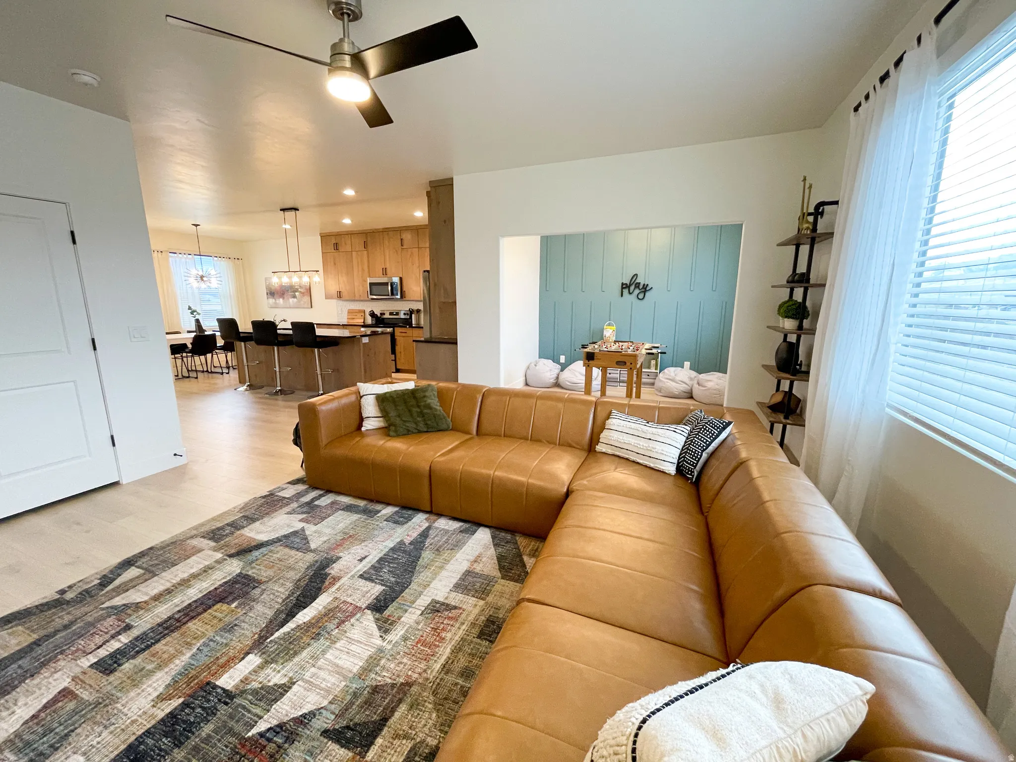 Recessed wall feature with paneling, light wood-finish flooring, ceiling fan with integrated lighting, kitchen island with seating, and pendant lighting
