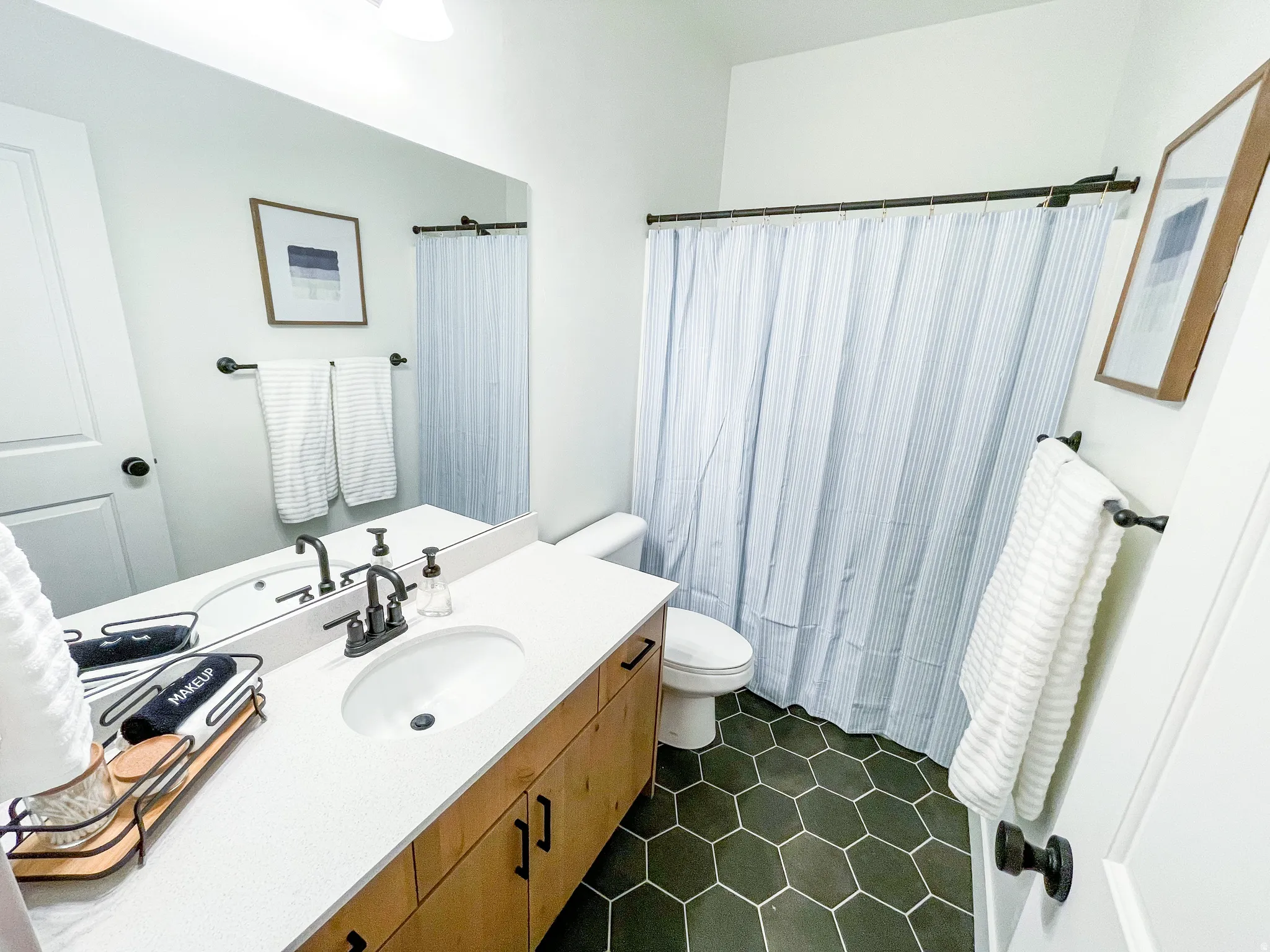 Hexagon tile flooring, single vanity with light-toned cabinetry, white countertop, oval undermount sink, and dark-finish fixtures