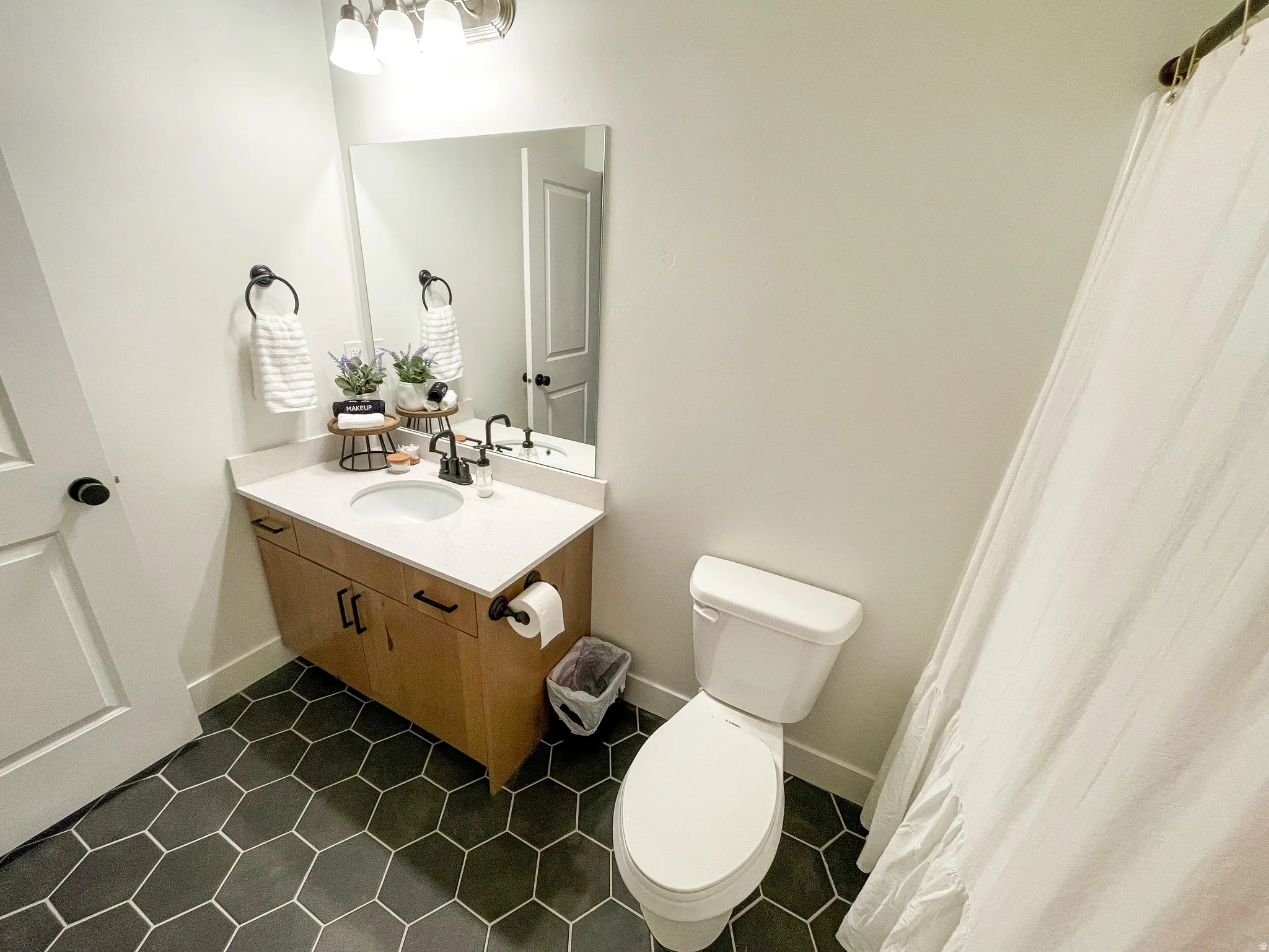 Bathroom with hexagon floor tiling, wood-finish vanity, light-colored countertop, and a contemporary vanity light fixture