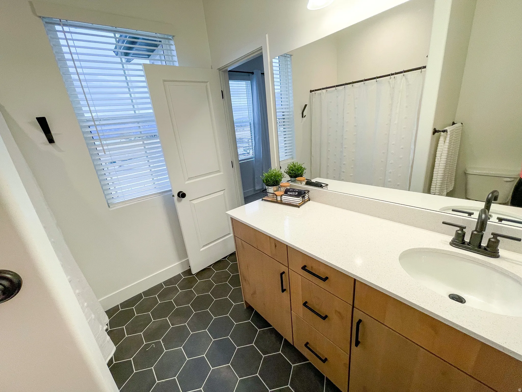 Hexagonal floor tiling, wood-finish vanity with drawer storage, white countertop, integrated sink, and dark bronze fixtures