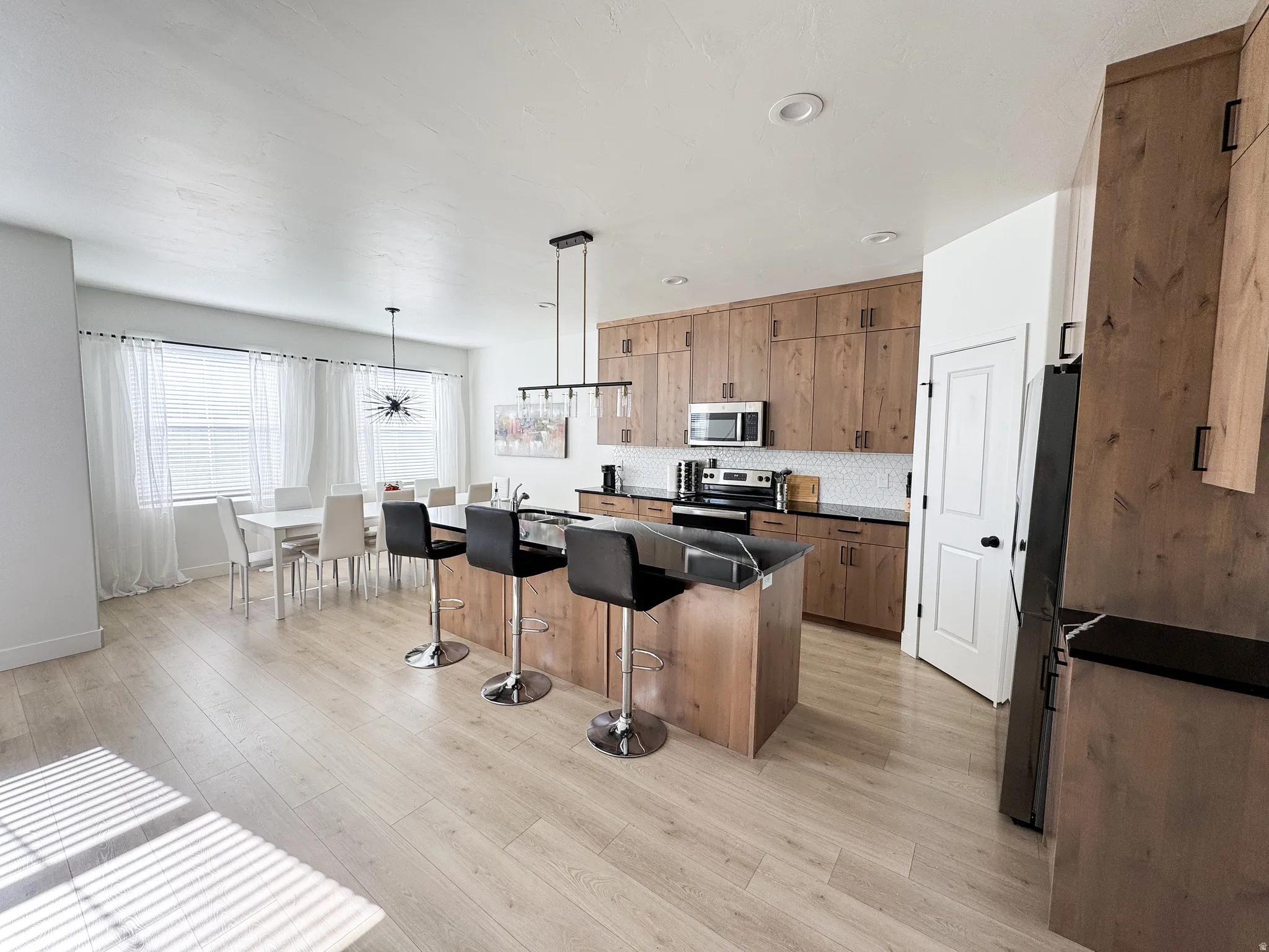 Wood-finish flooring throughout, kitchen featuring wood cabinetry, stainless steel appliances, and dark countertops, dining area with modern lighting
