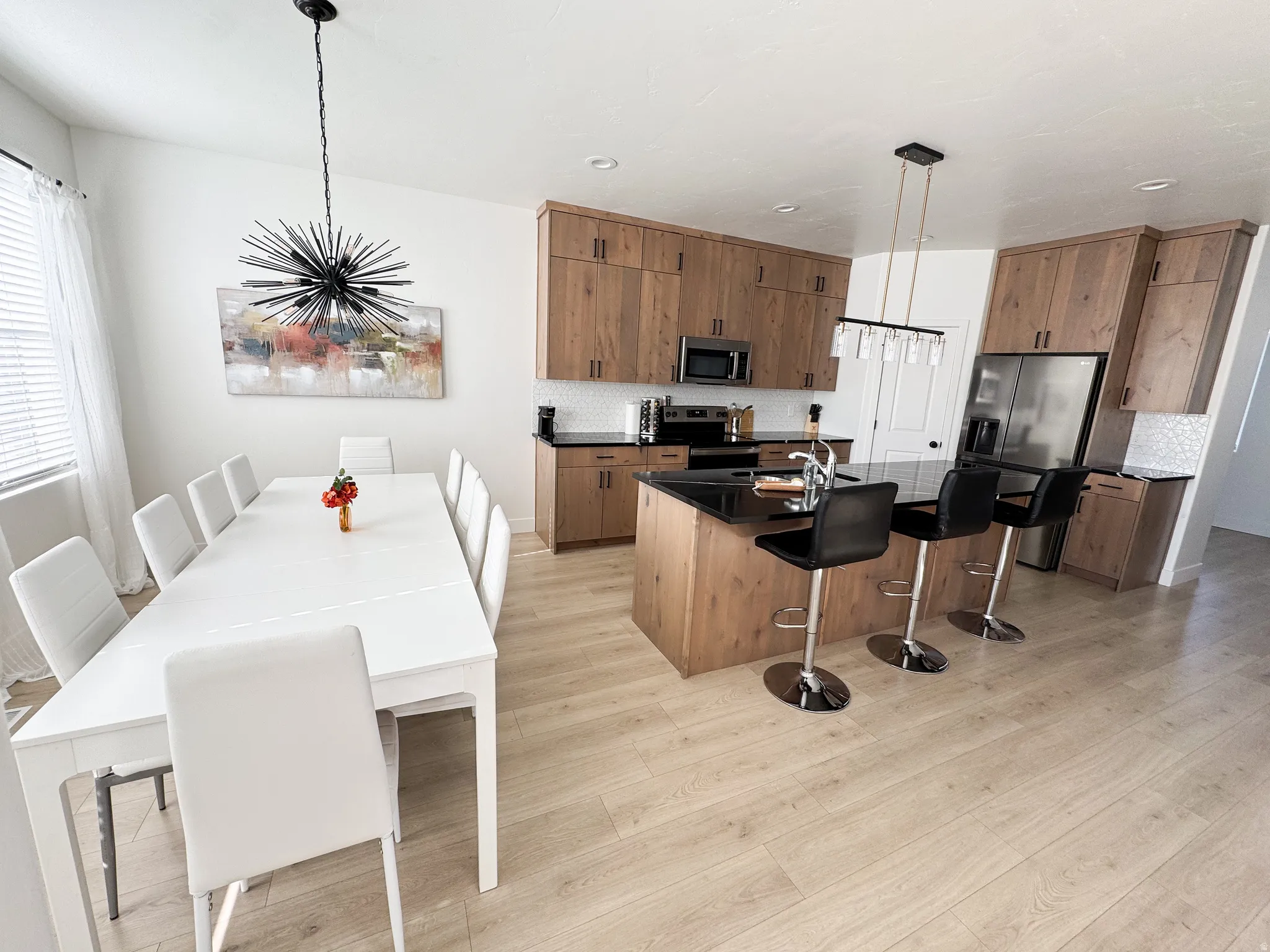 Open-concept kitchen and dining area featuring light wood-finish flooring, dark countertops, and a kitchen island with seating