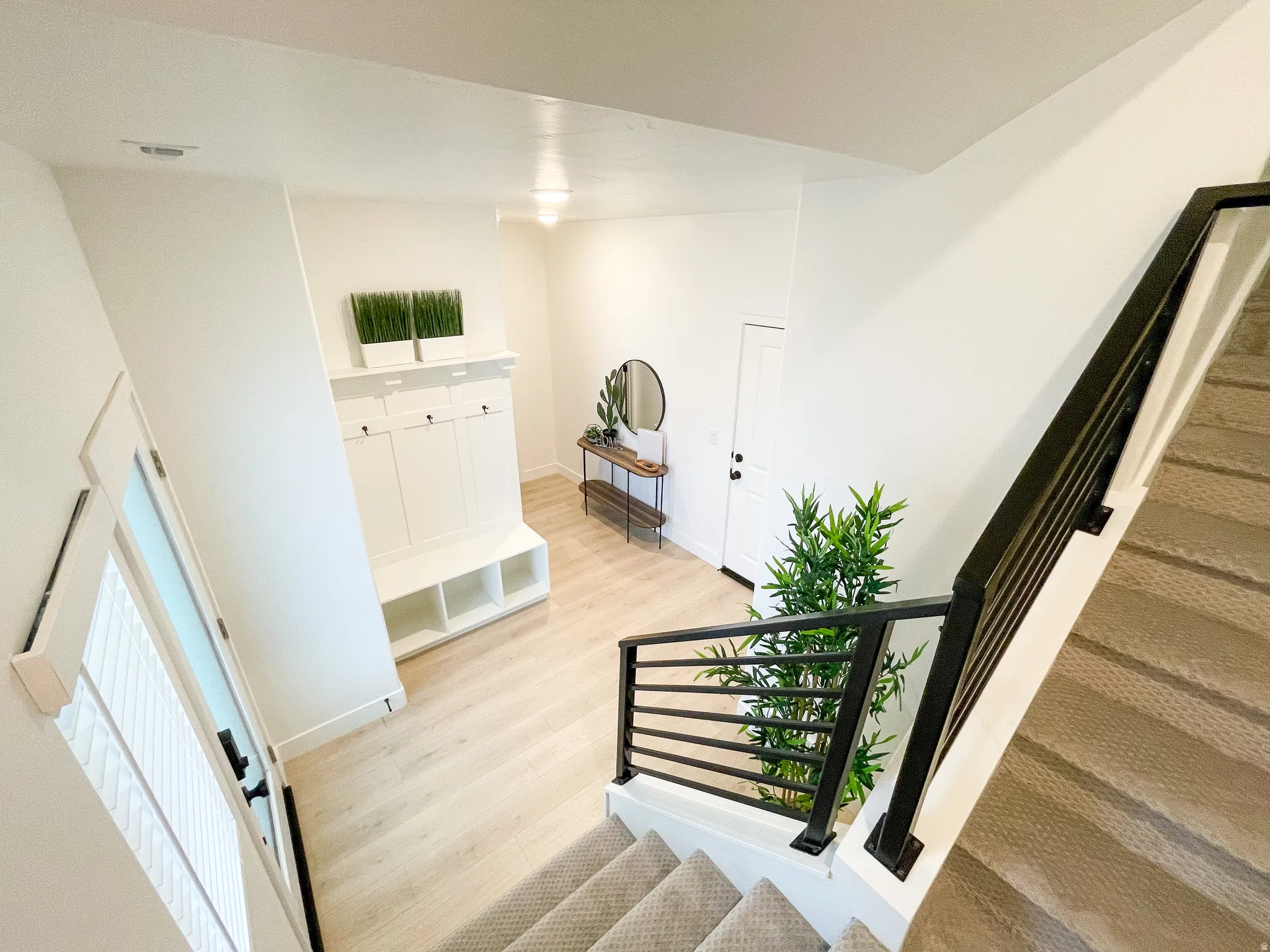 Wood-finish flooring, white walls, built-in hall tree with open shelving, dark metal stair railing, and a light-colored carpeted staircase