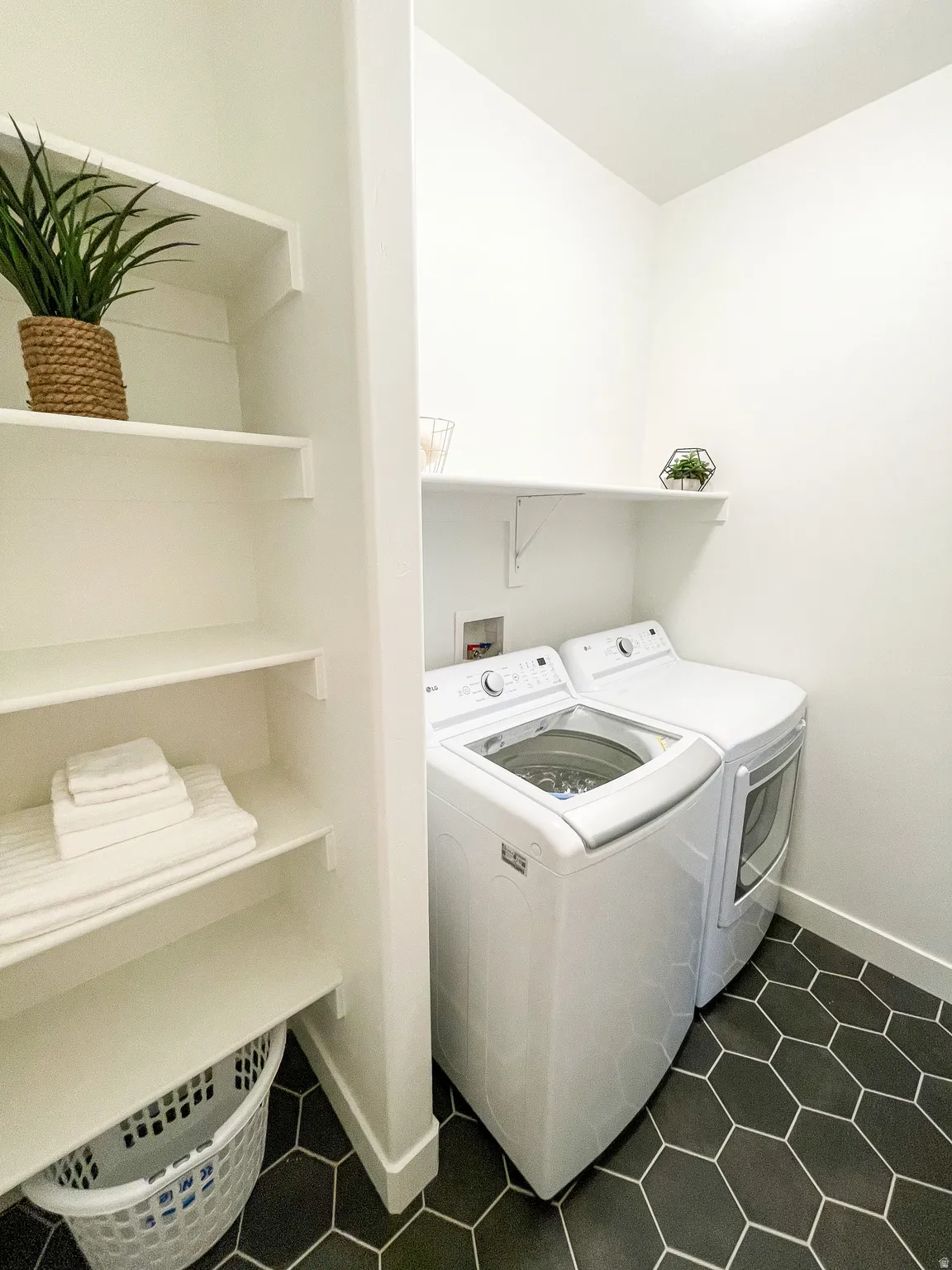Laundry area featuring dark hexagonal floor tiling, built-in shelving, and a wall-mounted shelf