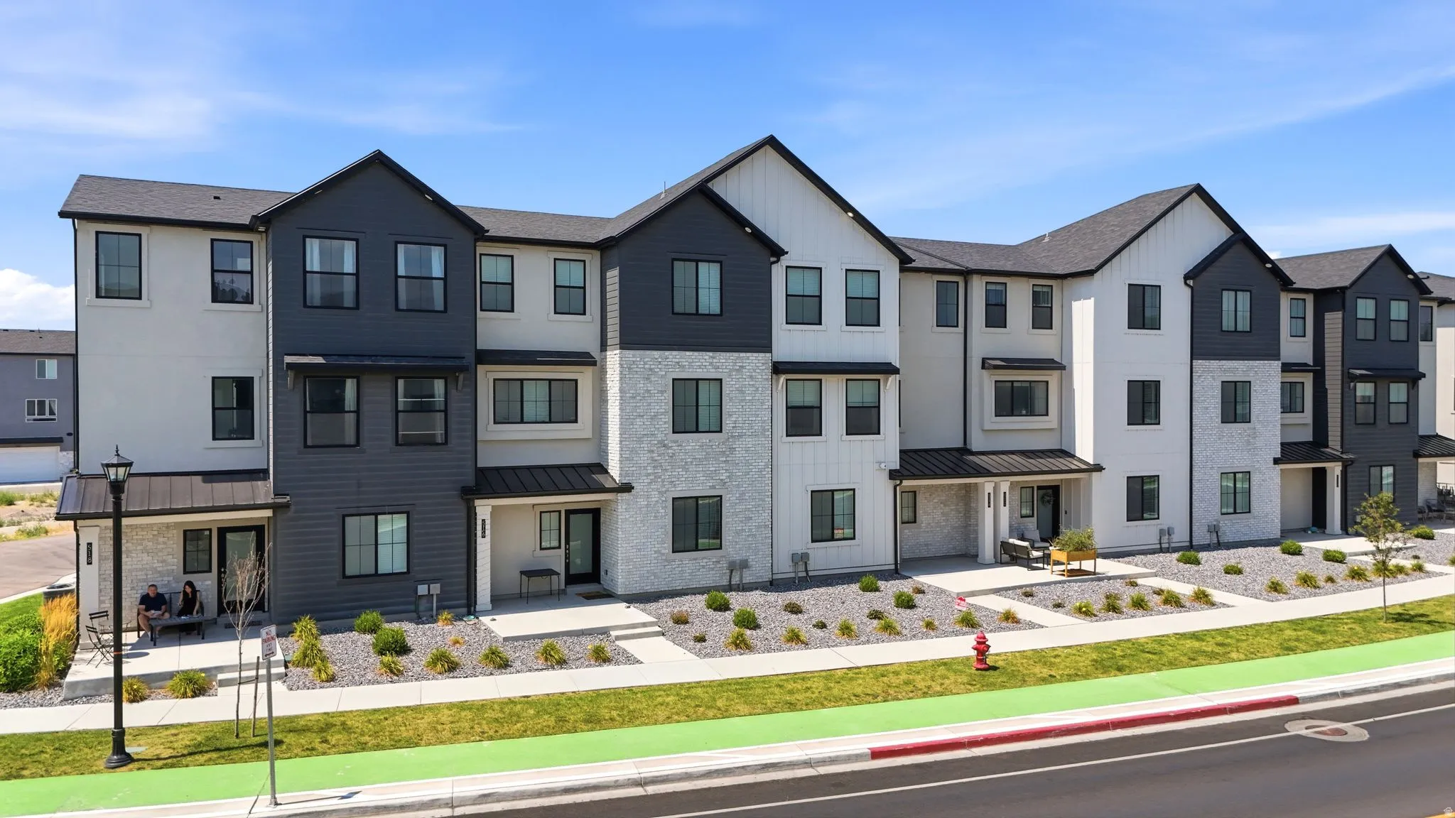 Multi-level townhome exterior featuring varied siding materials, black-framed windows, and covered entryways