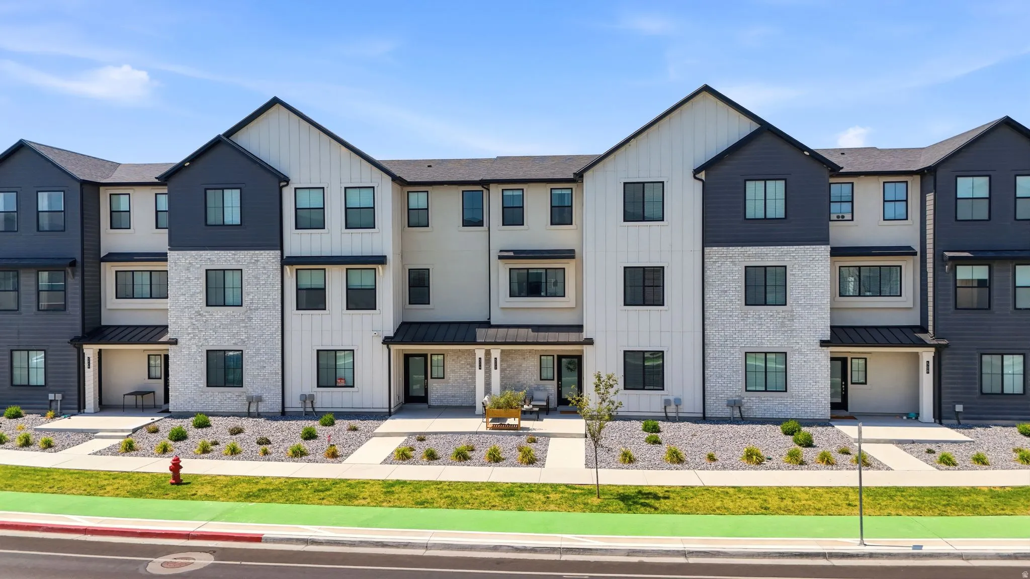 Modern multi-story facade featuring dark-framed windows, vertical white siding, and light-toned stone accents