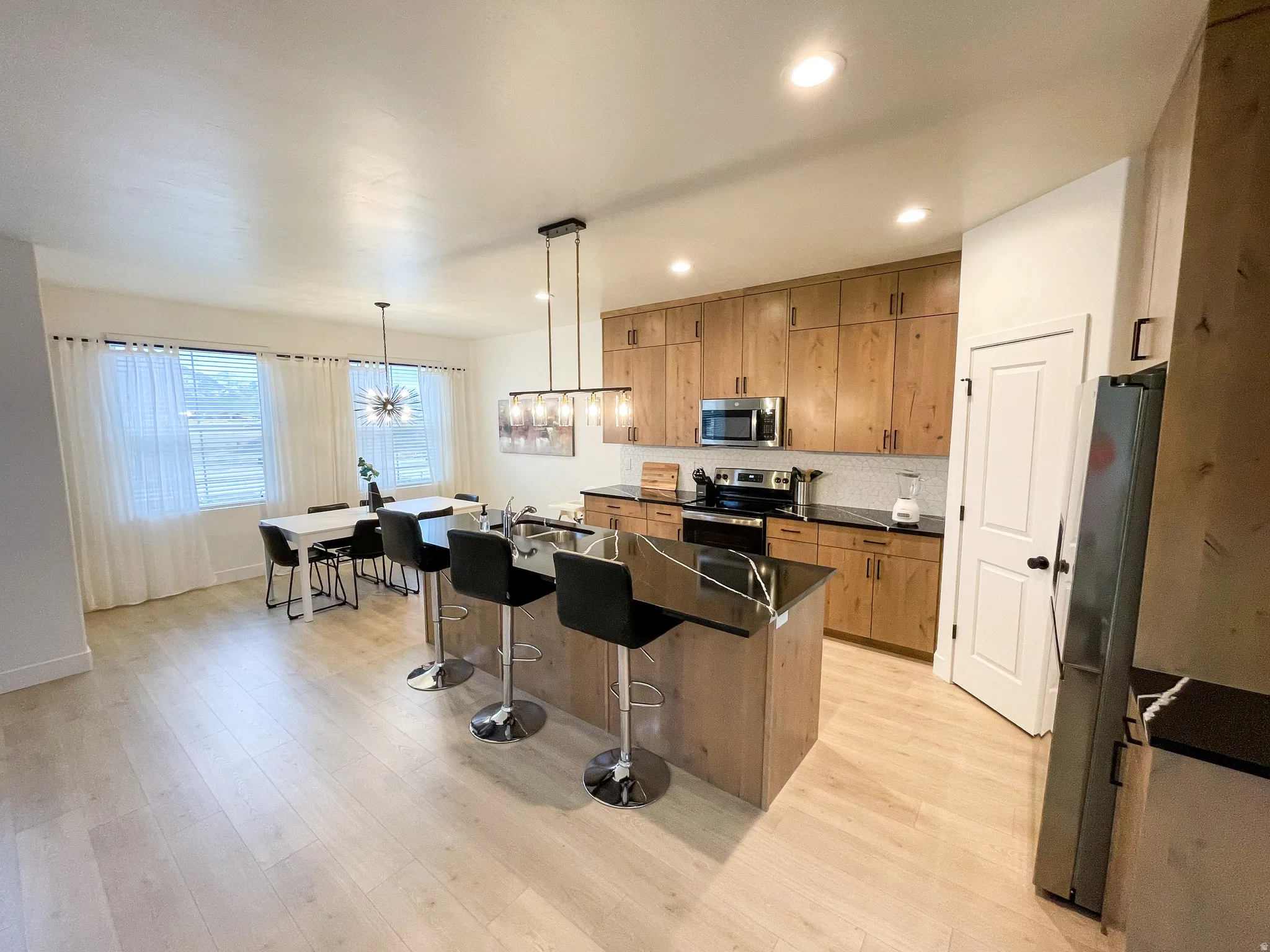 Contemporary kitchen with a central island, light wood-finish cabinetry, stainless steel appliances, dark countertops, and recessed lighting