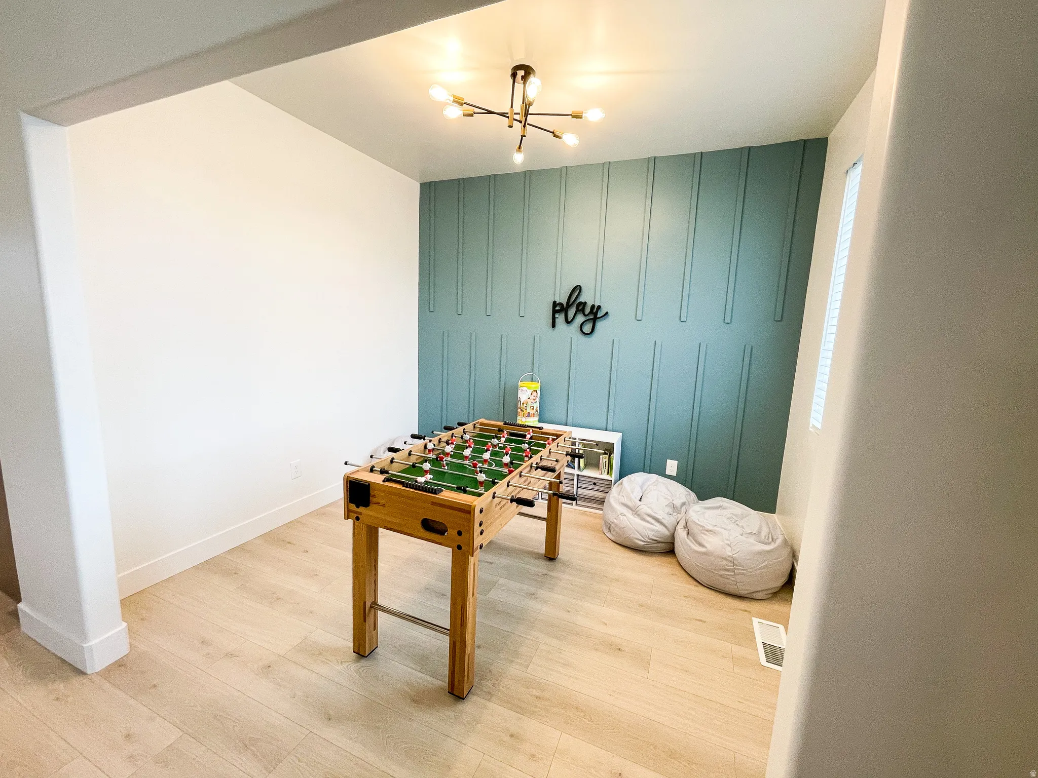 Recessed room featuring a contemporary chandelier, accent wall with vertical paneling, light wood-finish flooring, and a recessed window