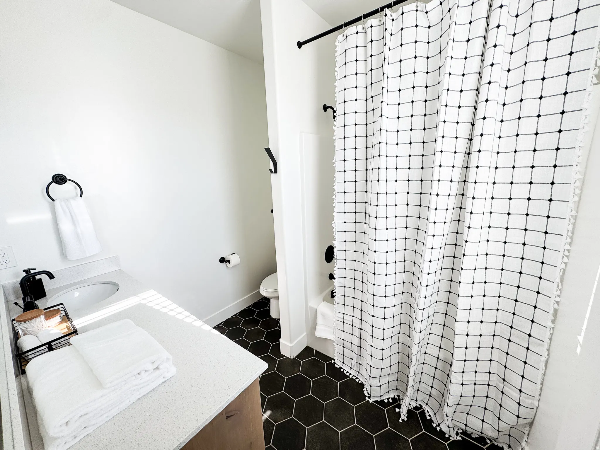 Hexagonal floor tiling, white walls, black fixtures, built-in vanity with countertop, and a shower/tub combination