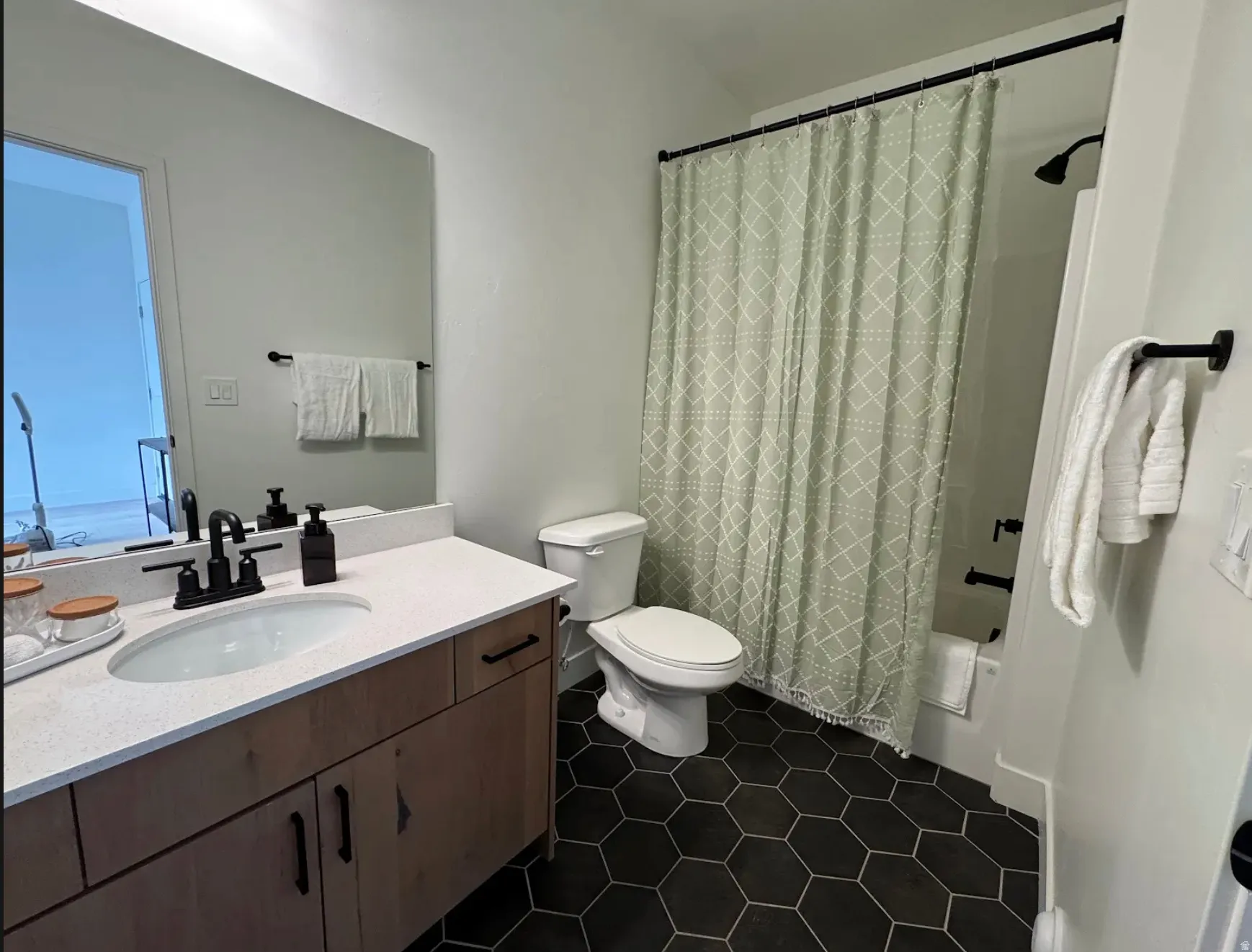 Modern bathroom featuring hexagonal floor tiles, a wood-finish vanity with a white countertop and oval sink, and matte black fixtures