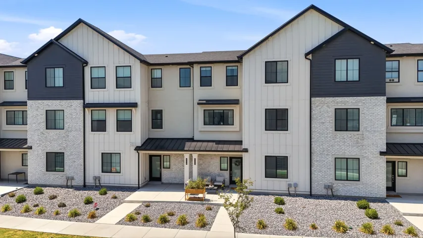 Modern townhouse exterior featuring white vertical siding, light gray brick, black horizontal siding accents, dark-framed windows, and a covered entry