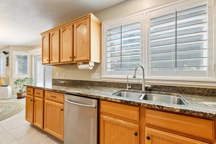 Kitchen featuring wood cabinetry, a double basin stainless steel sink, a stainless steel dishwasher, and a stone-finish countertop