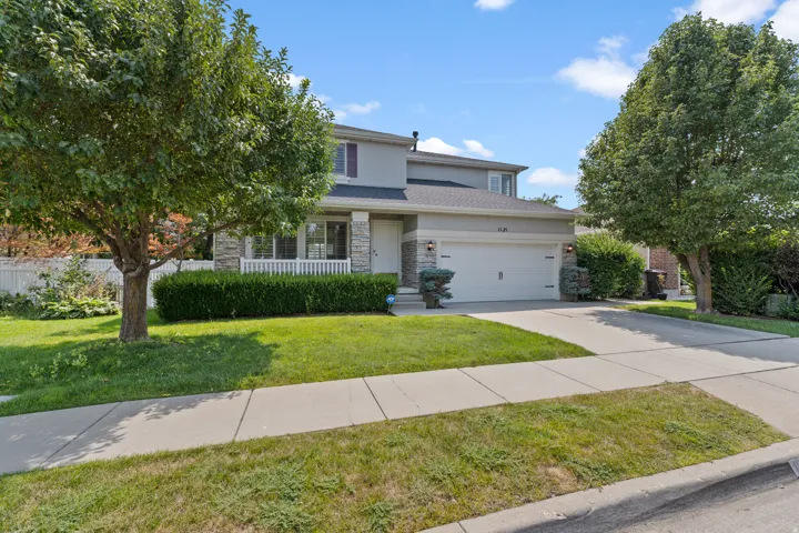 Two-story stucco and stone-clad residence with an attached two-car garage, mature front yard landscaping, a covered porch, and a concrete driveway