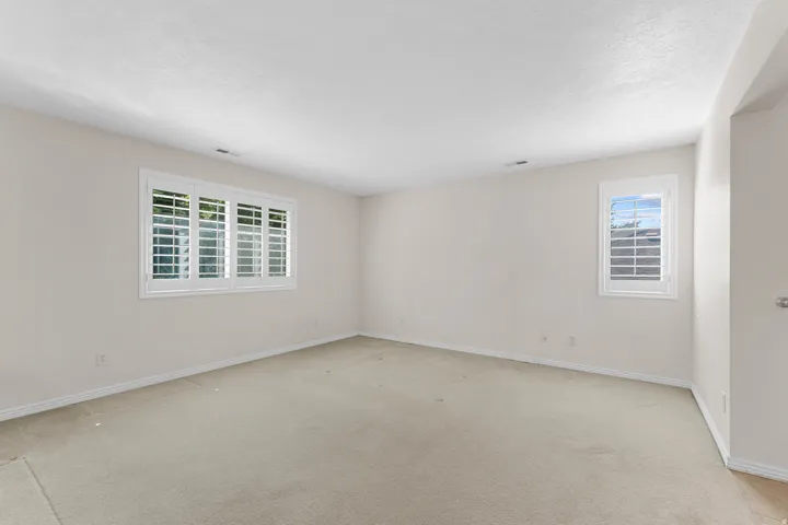 Carpeted room with two windows featuring white plantation shutters and light-colored walls