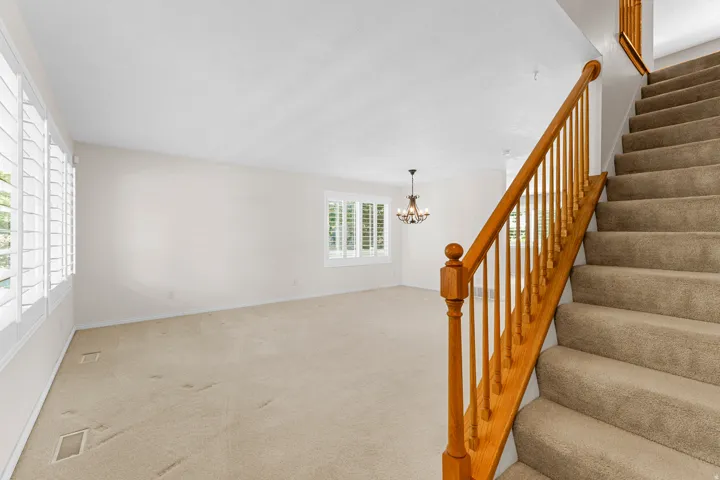 Expansive room with neutral carpeting, multiple windows featuring plantation shutters, and a chandelier lighting fixture