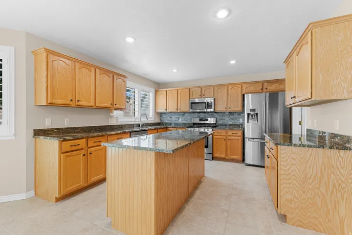 Kitchen featuring wood cabinetry, stone countertops, a tile backsplash, and stainless steel appliances