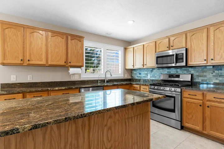 Kitchen featuring wood cabinetry, stone countertops, a tile backsplash, stainless steel appliances, and a central island