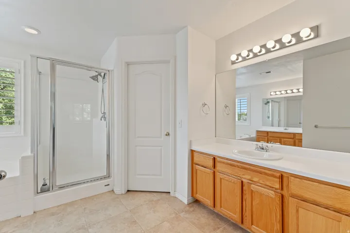Glass-enclosed shower, built-in bathtub, light wood-finish vanity with an integrated sink, large mirror, and tile flooring