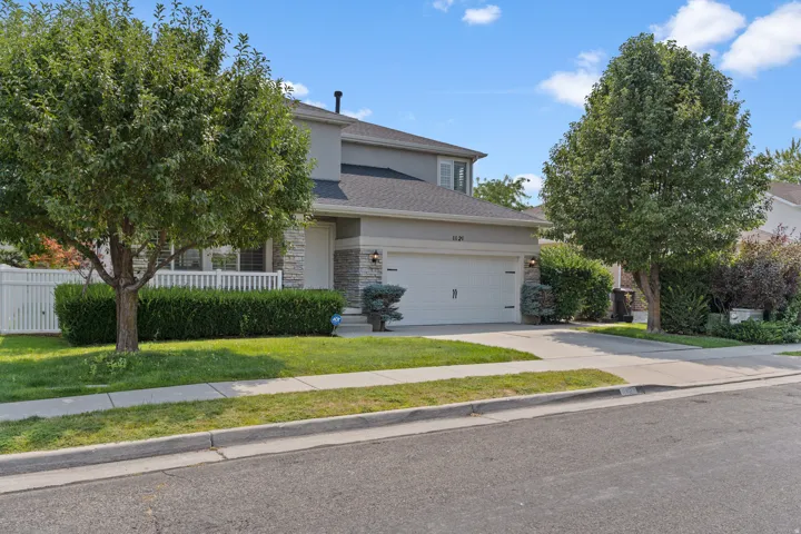 Two-story residence with a two-car garage, stone facade accents, and a front lawn with mature trees