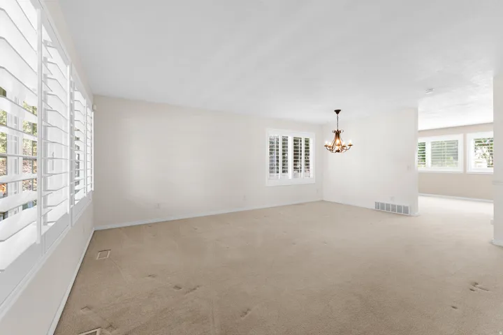 Warm neutral wall tones, large windows with white louvered shutters, and an ornate chandelier