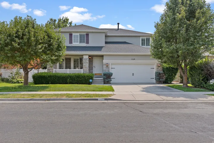 Two-story residence featuring a two-car garage, covered porch, partial stone façade, and mature landscaping