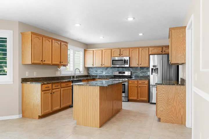 Kitchen featuring wood cabinetry, stainless steel appliances, granite countertops, a center island, and tile flooring