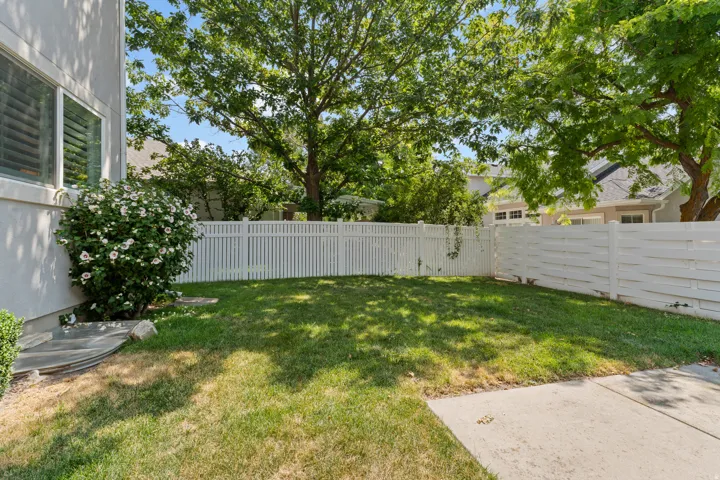 Enclosed yard with a combination of privacy fencing and picket fencing, featuring a concrete patio, green lawn, and mature trees
