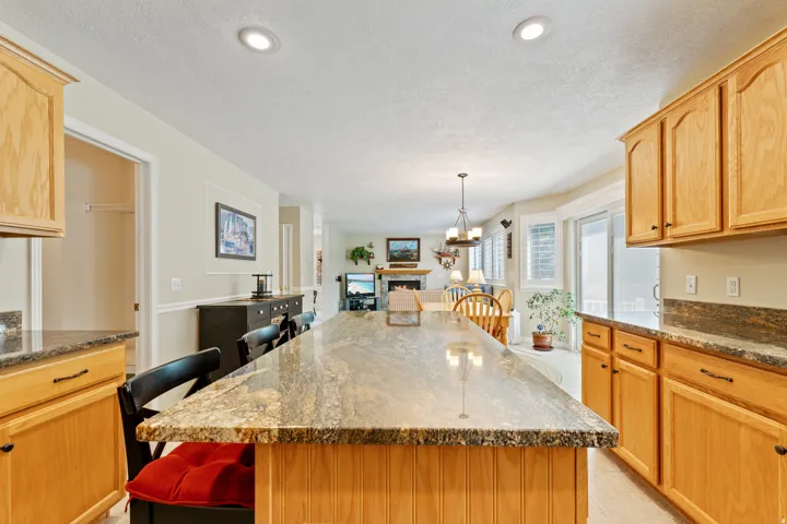 Kitchen island with an extended granite countertop, light wood cabinetry, and recessed lighting