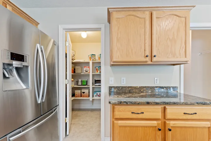 Stainless steel refrigerator, wood-finish cabinetry, granite countertop, kitchen pantry with shelving, and tile flooring