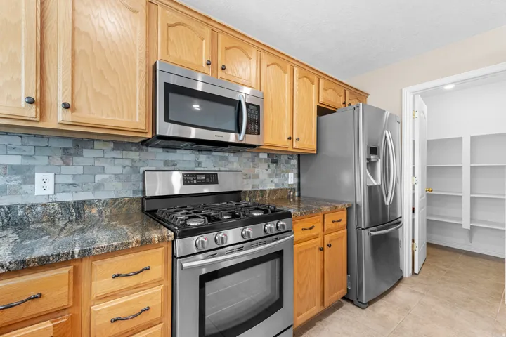 Kitchen with wood cabinetry, stainless steel appliances, stone countertops, and a tile backsplash