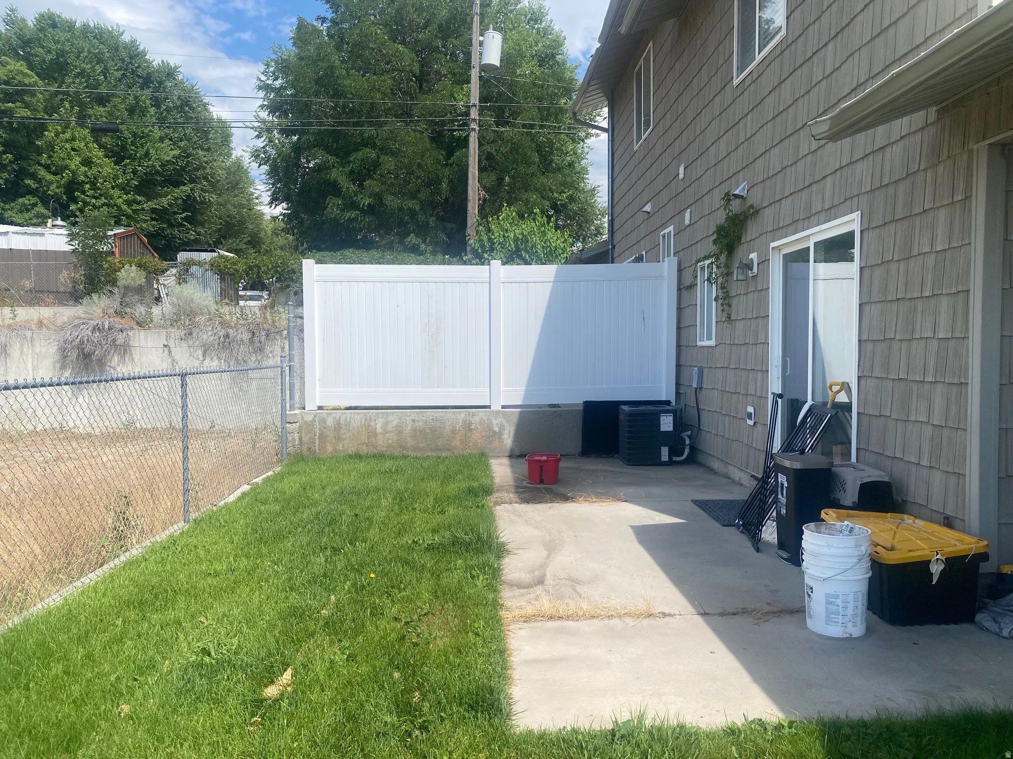 Exterior featuring horizontal siding, white vinyl fencing, a concrete patio, and a grass area