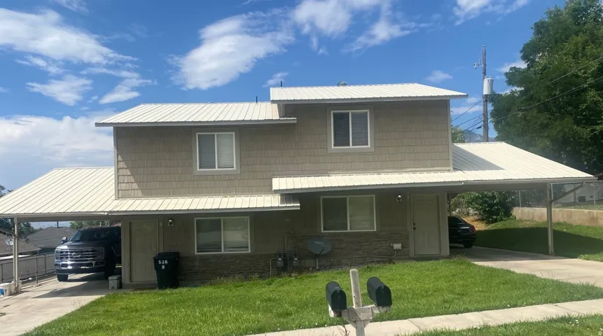 Two-story duplex with metal roofing, upper level shake siding, lower level stone veneer, and two carports