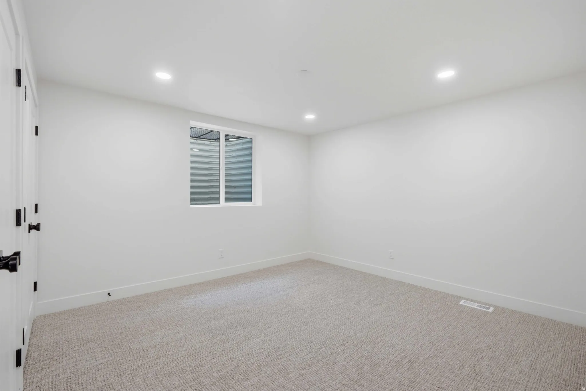 Recessed lighting, white walls, light-toned carpeting, white trim, and a white-framed window