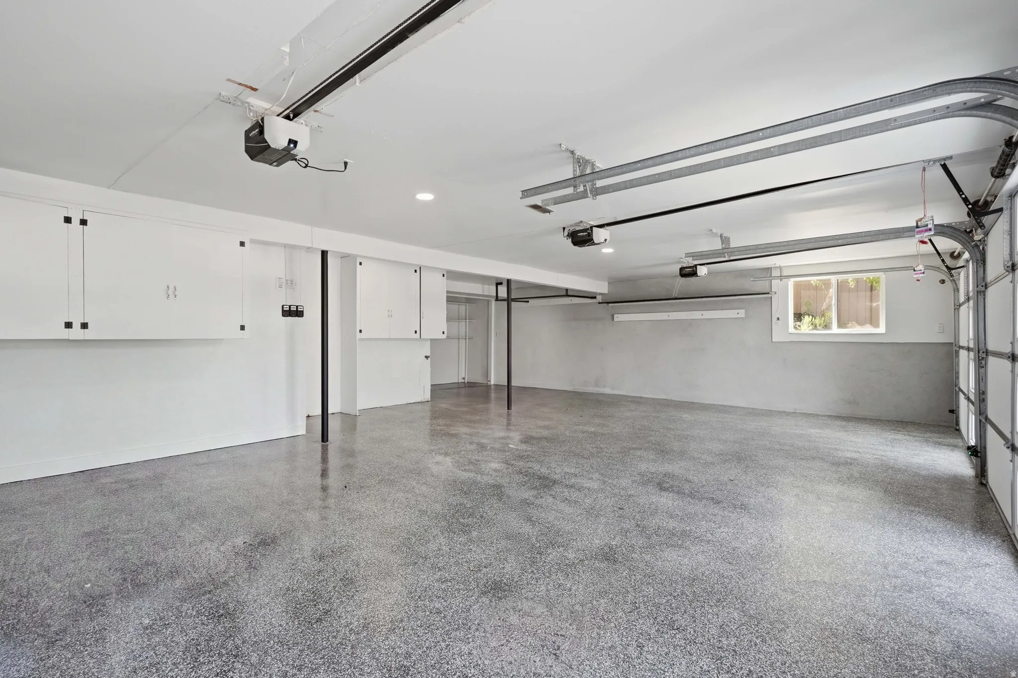Expansive garage with epoxy flooring, white built-in cabinetry, and integrated overhead lighting