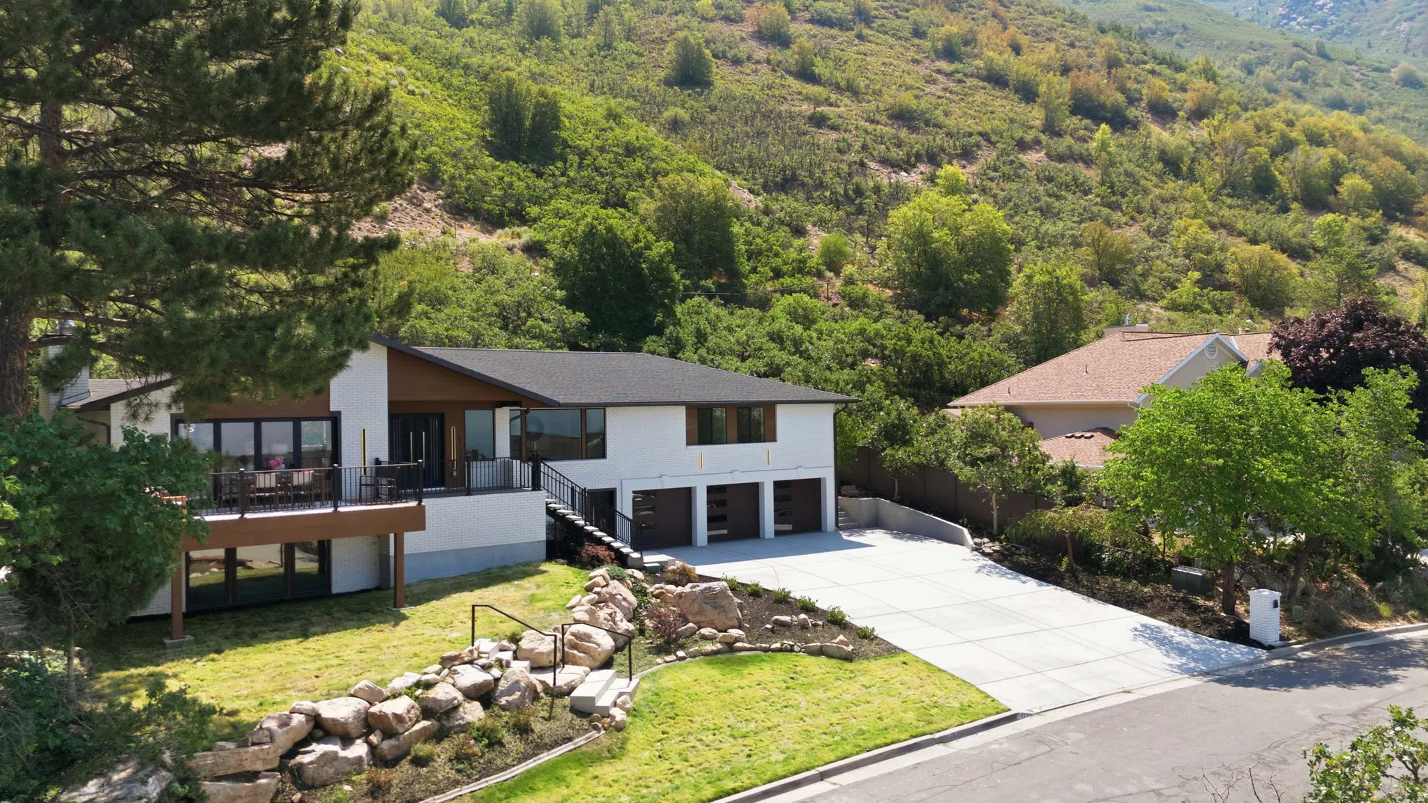 Contemporary residence featuring a spacious deck with dark railing, a three-car garage, and a concrete driveway