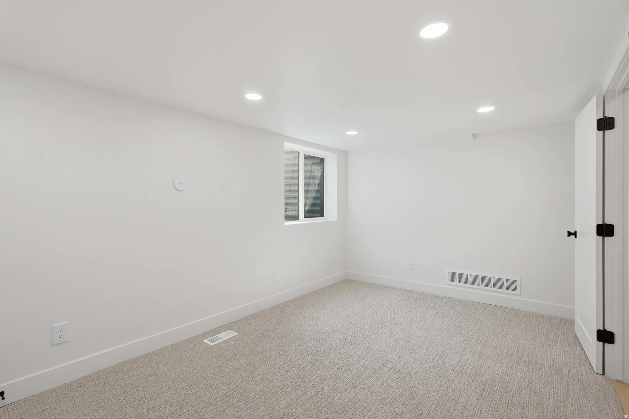 White walls, recessed ceiling lighting, light-toned carpeting, and a white-framed window