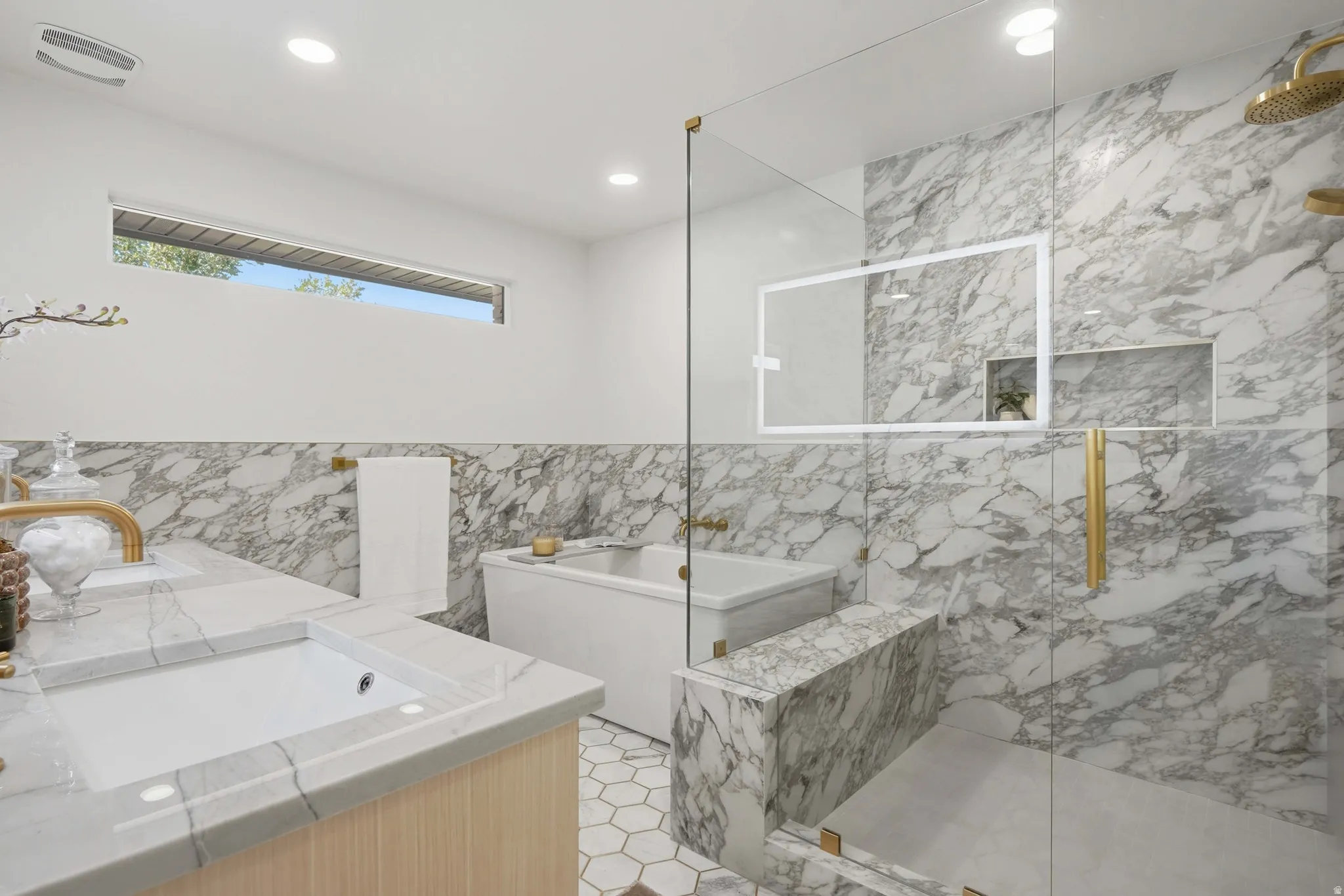 Recessed lighting, large soaking tub, glass-enclosed shower, integrated shower niches, and gold-tone fixtures