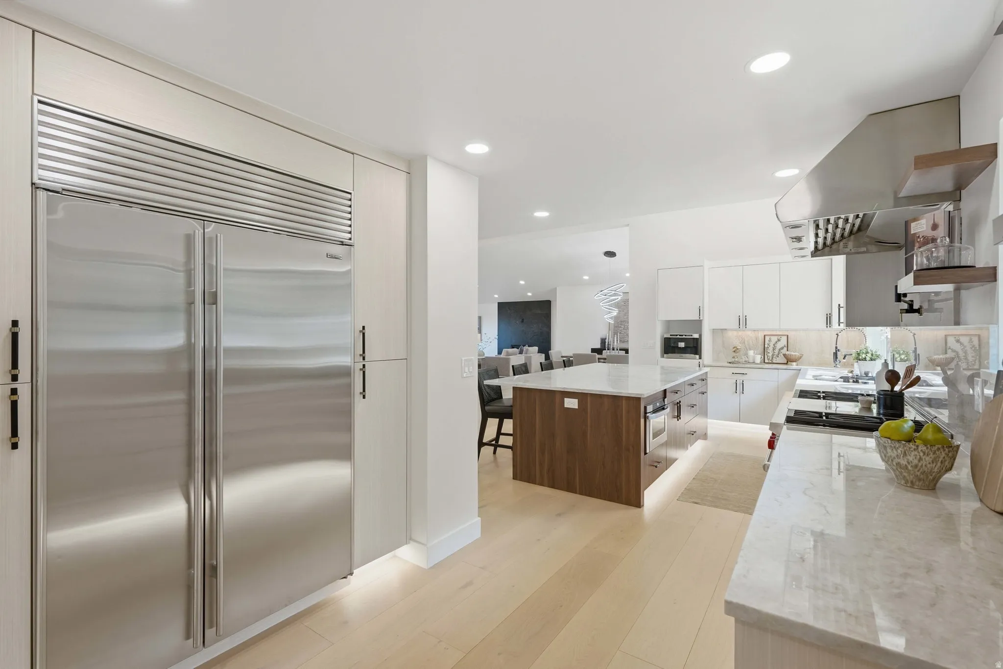 Gourmet kitchen featuring a built-in stainless steel refrigerator, white cabinetry, a large center island with wood-finish paneling, light wood-finish flooring, and recessed lighting