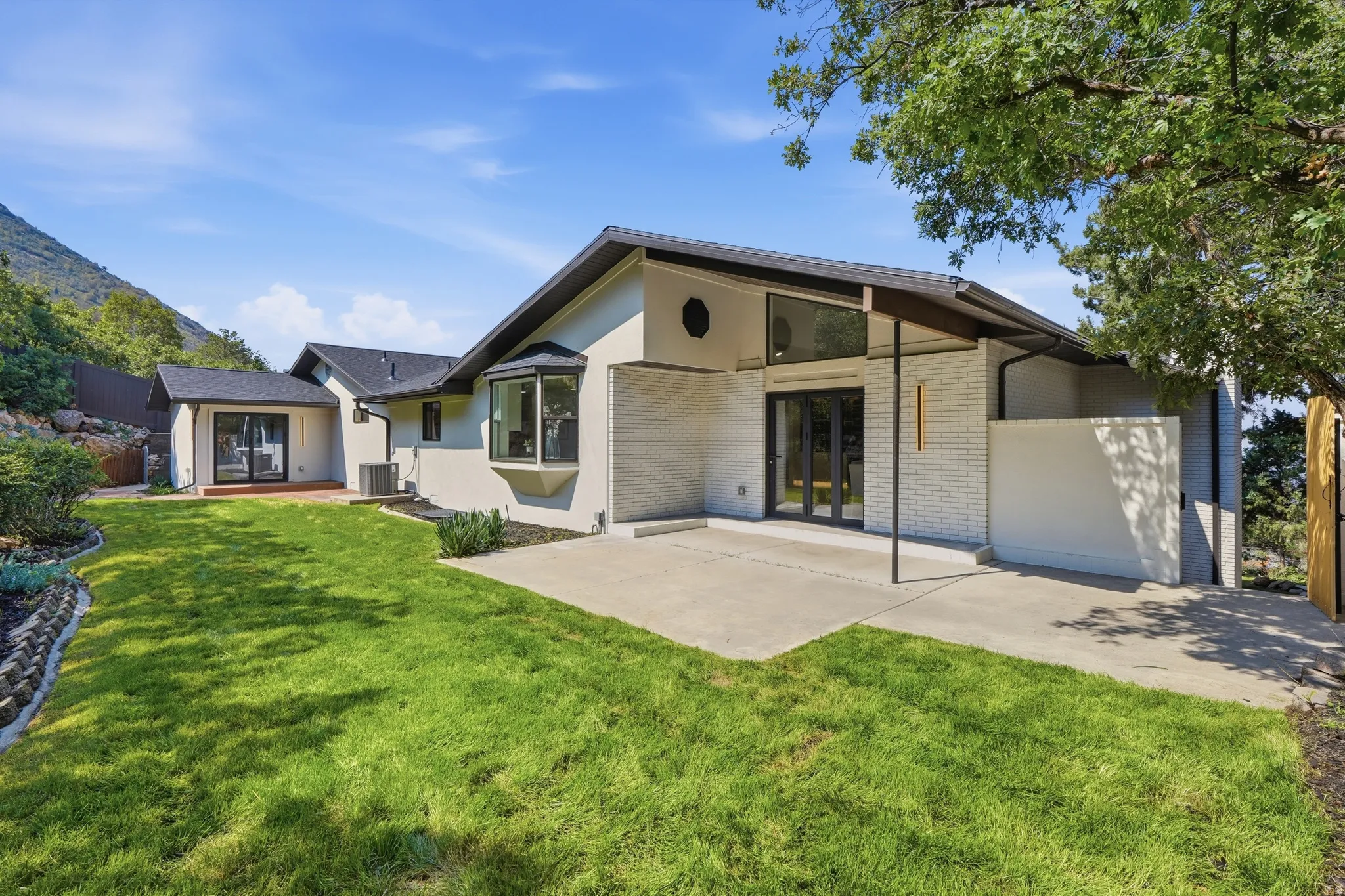 Expansive lawn with a concrete patio, contemporary exterior finishes, and a bay window
