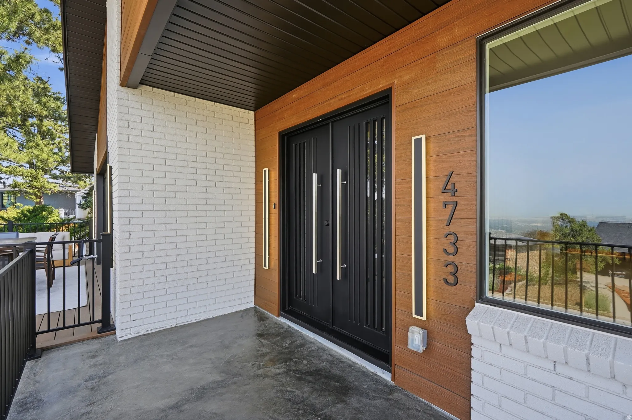Modern exterior featuring a dark wood-finish soffit, white brick siding, wood-look wall panels, and a large picture window