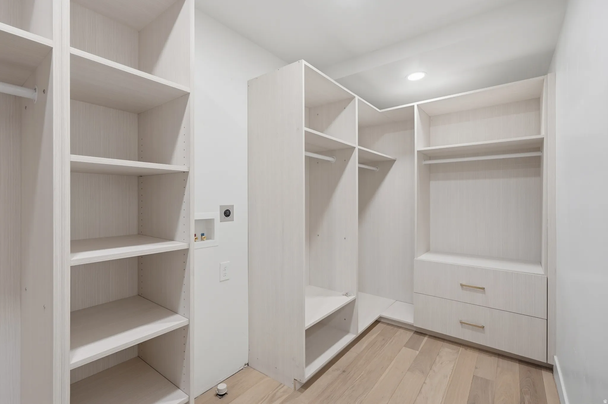 Custom closet system with integrated shelving, multiple hanging rods, and built-in drawers with gold-toned hardware